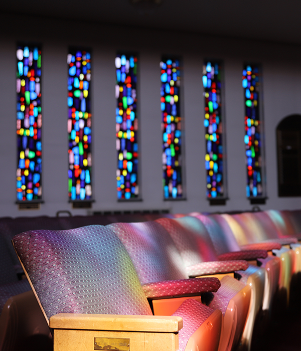 rows of empty seats in a room with stained-glass windows